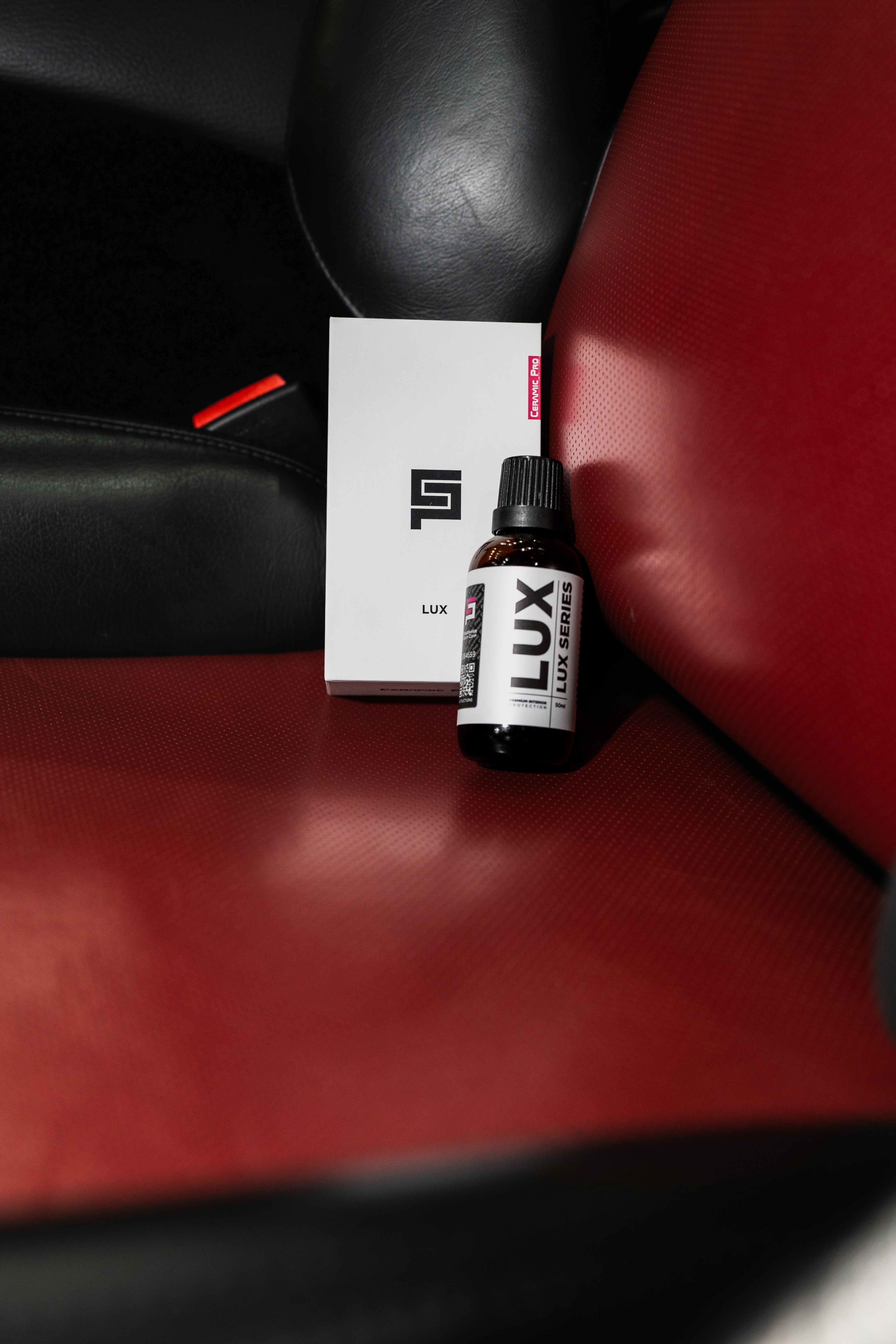 Flacon Ceramic Pro LUX sur le siège en cuir rouge bordeaux d'une Porsche 911, détail d'intérieur d'exception