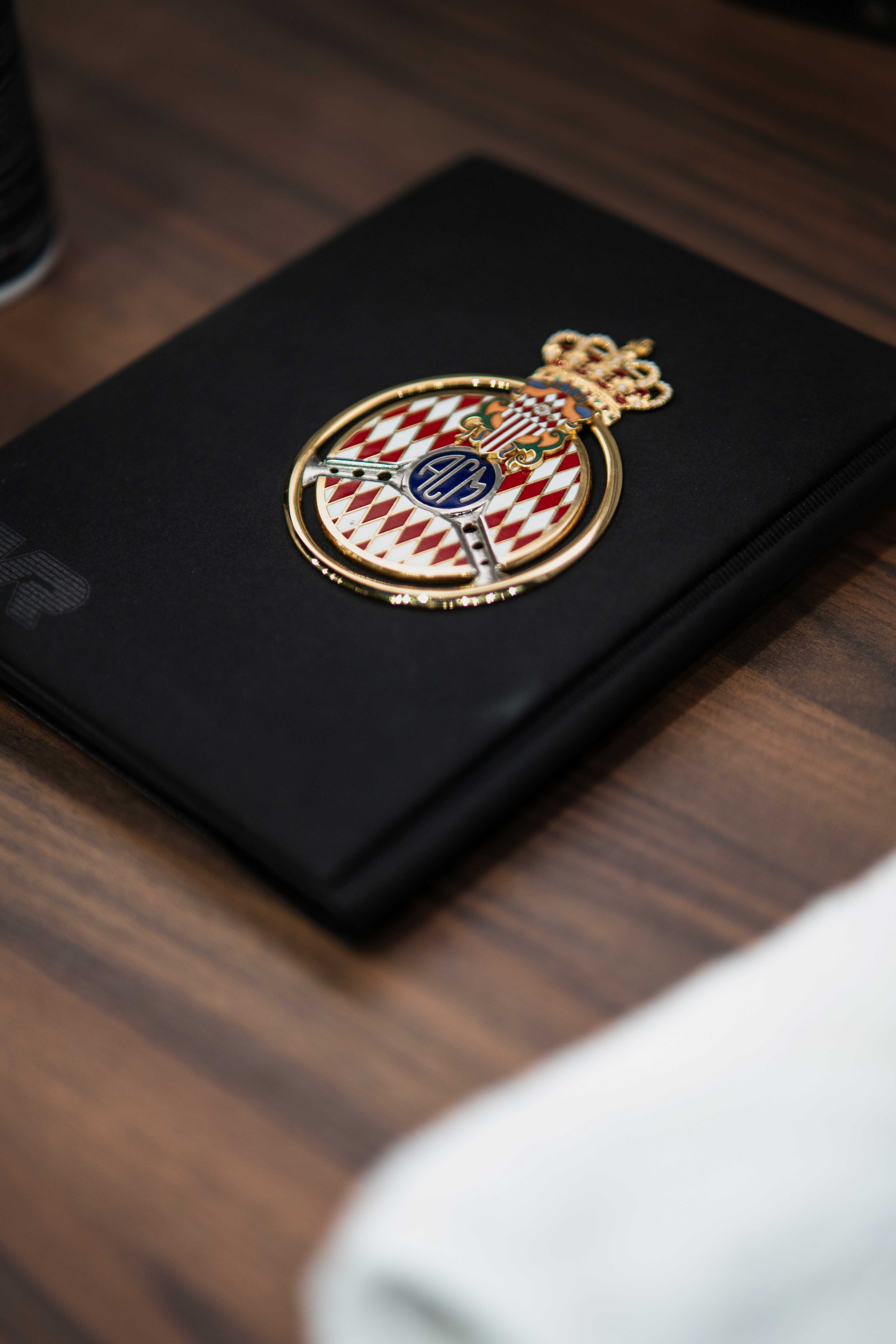 Badge de concours d'élégance posé sur un carnet noir, symbole d'un patrimoine automobile transmis